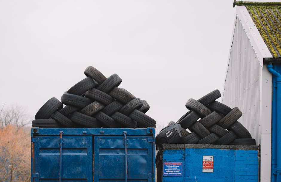 A large pile of mixed household and commercial waste, including cardboard boxes, plastic bags, paper debris, and various discarded packaging materials, is accumulated on a paved sidewalk area. The was